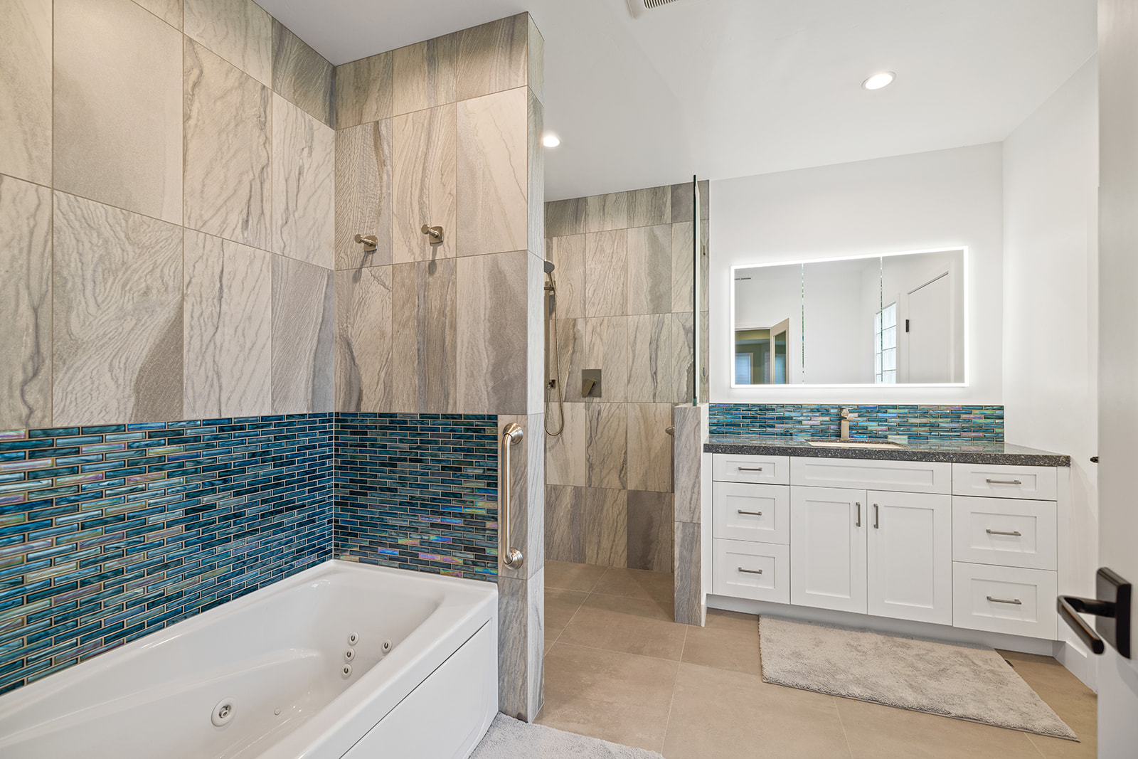 Bathroom remodel with soaking tub and LED mirror Remodeled bathroom with soaking tub, blue glass mosaic band, white vanity, and backlit LED mirror
