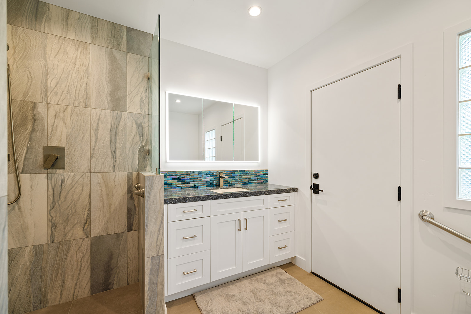 Bathroom vanity with backlit mirror Bathroom remodel with white shaker vanity, dark stone countertop, and backlit LED mirror