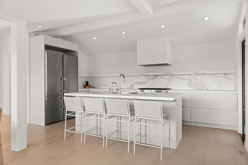White kitchen remodel — Carmel-by-the-Sea Remodeled white kitchen with marble waterfall island, stainless appliances, and vaulted ceiling in Carmel-by-the-Sea