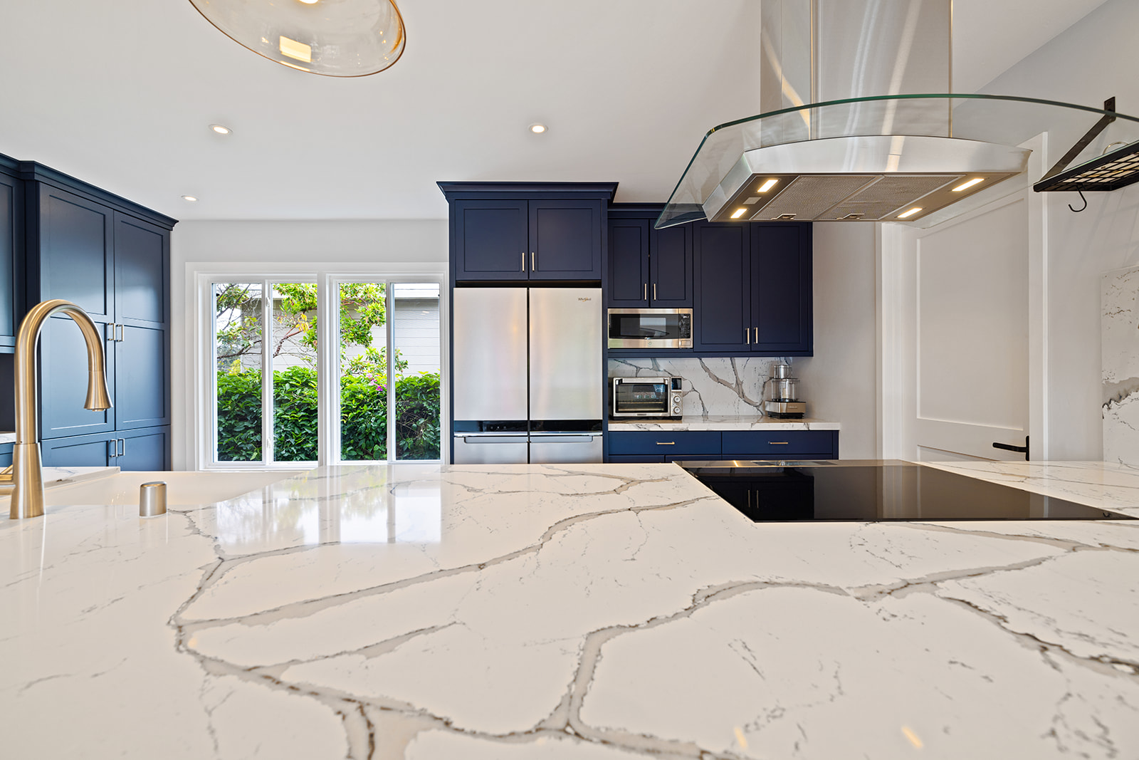 Kitchen island with stainless range hood Remodeled kitchen with quartz island, stainless range hood, and navy blue cabinetry